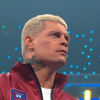 Cody Rhodes appears on WWE SmackDown, showcasing a serious expression and styled hair, wearing a maroon jacket with a logo. The background features colorful lights and a wrestling ring environment.