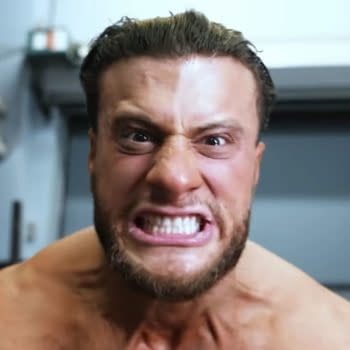 A man with short hair and a fierce expression, showing his teeth, appears agitated as he addresses the camera. He is shirtless with visible muscle definition.
