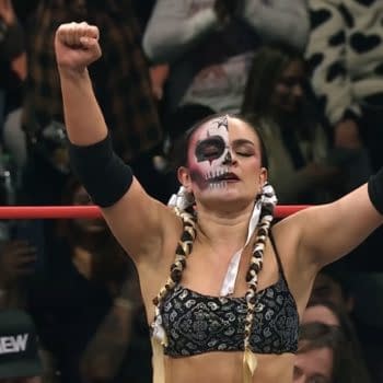 Thunder Rosa, an AEW wrestler, stands triumphantly with her arms raised, showcasing her striking face paint and braided hair, while fans cheer in the background.
