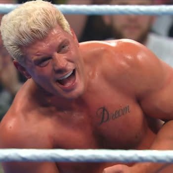 Cody Rhodes is celebrating after winning the WWE Championship, grinning widely with a tattoo visible on his chest that reads 'Dream'. The background shows cheering fans watching the moment unfold.
