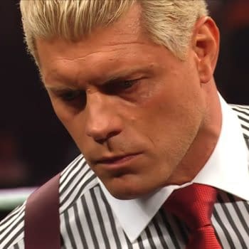 Cody Rhodes appears contemplative in the wrestling ring, wearing a striped shirt and red tie while holding a championship belt. He looks serious, addressing emotional themes.