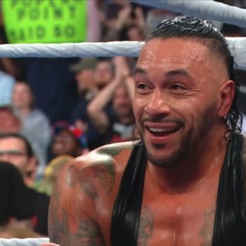 Damian Priest smiles broadly, expressing delight after winning his match during WWE SmackDown, with a cheering crowd in the background.