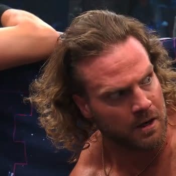 Hangman Adam Page shows a tense expression while reacting to the end of a wrestling event, revealing a mix of emotion and surprise. A blurred figure is partially visible behind him.