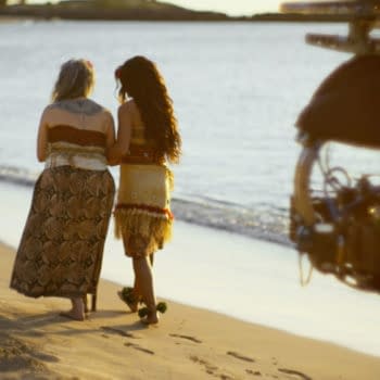MOANA Behind-the-scenes photo from Disney's live-action Moana, featuring Rena Owen and Catherine Laga'aia walking along the beach.
