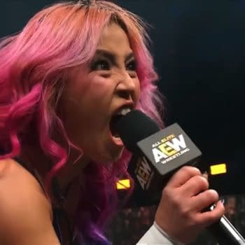Mina Shirakawa, with vibrant pink hair, passionately challenges her opponent on stage, holding a microphone labeled with the AEW logo.
