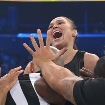 Ronda Rousey laughing and being held back by officials during an AEW Revolution event. The scene captures her excitement as she challenges Toni Storm.