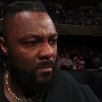 A close-up of a man with a serious expression, showing frustration or disbelief while watching AEW Dynamite. Fans and commentators can be seen in the background.