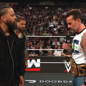 The Usos confront CM Punk in the ring during an episode of WWE Raw, with a captivated audience in the background and CM Punk holding a microphone and a championship belt.