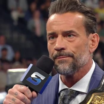 CM Punk speaks directly to Cody Rhodes while holding a championship belt, with a crowd visible in the background. Both wrestlers are engaged in a tense moment during WWE SmackDown.