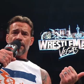 A professional wrestler passionately addresses the crowd while holding a microphone, with the WrestleMania Las Vegas logo prominently displayed in the background.