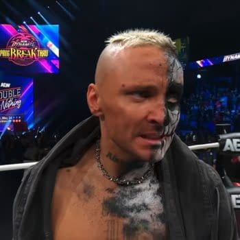 Darby Allin reacts with a serious expression as he listens to another wrestler, MJF, during an AEW Dynamite event. The backdrop features vibrant colors and promotional graphics for AEW's Spring Breakthru and Double or Nothing events.
