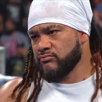 Jacob Fatu stands in the ring on WWE SmackDown, wearing a white head covering and sleeveless top with a stern expression.
