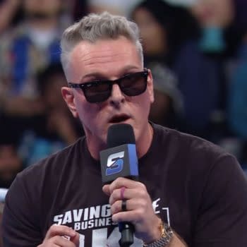 Pat McAfee speaks into a microphone while wearing sunglasses, standing in a wrestling ring. The audience is visible behind him, reacting to his taunts directed at the WWE Universe.