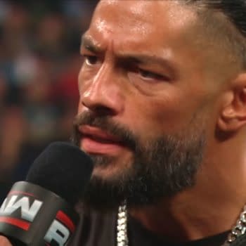 Roman Reigns speaks into a WWE microphone during a tense promo on Raw, with his championship belt visible on his shoulder.