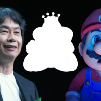 Shigeru Miyamoto smiles while standing next to a cartoon character resembling Mario, the iconic figure from Nintendo, with a blurred background. The image captures a moment from an E3 gaming conference.