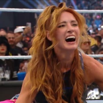 A woman's face filled with joy and excitement, her long, wavy red hair framing her smile. She is surrounded by an enthusiastic crowd, celebrating a victory in a wrestling event.
