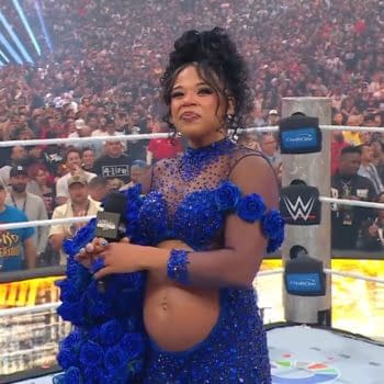 A woman stands in a wrestling ring wearing a stunning blue outfit adorned with flowers, holding a microphone. The audience is visible in the background, showcasing a vibrant WrestleMania atmosphere.