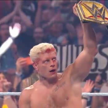 Wrestler Cody Rhodes, with a bloody face and a winning expression, raises the WWE Championship belt high above his head while a cheering crowd surrounds him.