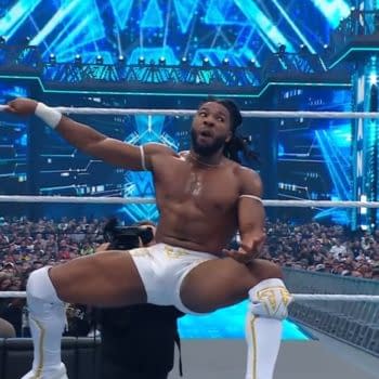 A wrestler celebrating in the ring at WrestleMania, wearing white trunks and striking a dynamic pose against a vibrant blue backdrop filled with lights and an enthusiastic crowd.