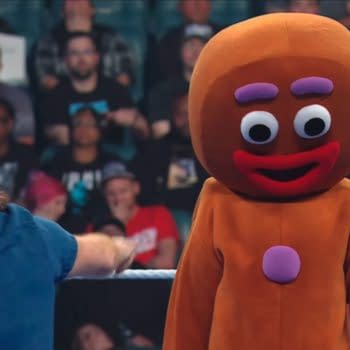 Sami Zayn points toward a person in a giant gingerbread man costume standing helplessly in the WWE ring. The crowd watches in the background.