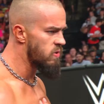 Austin Theory glares intensely in the WWE Raw ring, looking furious as the crowd watches in the background.