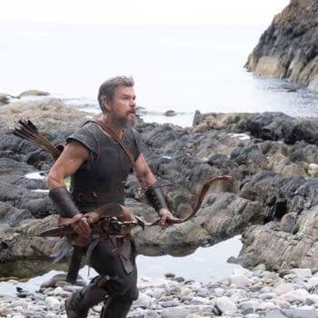 Matt Damon as Odysseus stands on a rocky shoreline holding a bow and arrows in The Odyssey.