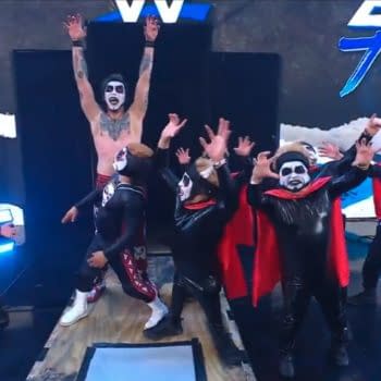 Danhausen stands on the WWE Backlash stage with several masked dancers or performers in black-and-red costumes, raising his arms in a celebratory pose.