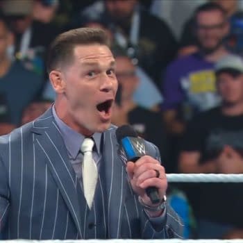 John Cena stands in the WWE ring in a striped suit, speaking excitedly into a microphone during a Backlash announcement. He appears to be unveiling the John Cena Classic.