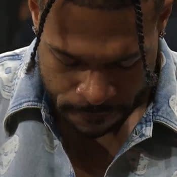 Kevin Knight looks down with a frustrated expression during AEW Double or Nothing, wearing a light denim shirt with skull patterns.