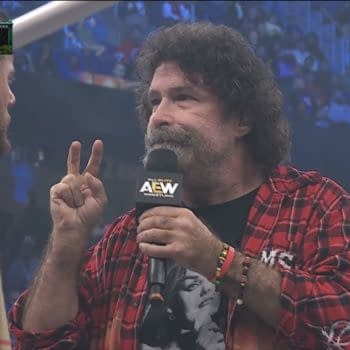 Mick Foley speaks into an AEW microphone while facing MJF and holding up two fingers at AEW Double or Nothing. The Buy-In pre-show crowd blurs in the background.