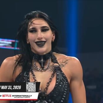 Rhea Ripley smiles in the WWE ring during Saturday Night’s Main Event, wearing dark ring gear and black makeup. A “Clash in Italy” promotional banner appears at the bottom of the screen.