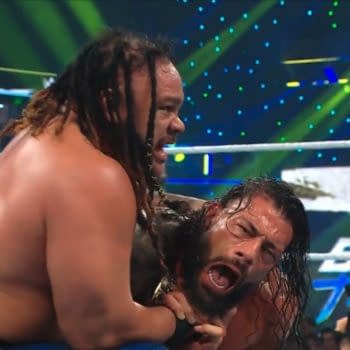 Roman Reigns is trapped in a brutal hold from Jacob Fatu during WWE Backlash. The tense ringside moment shows Reigns grimacing under heavy punishment.