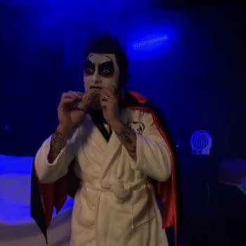 Danhausen, in face paint and a robe, eats a snack under blue lighting on WWE SmackDown.