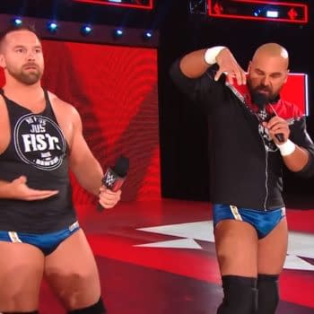 FTR stand in a WWE Raw ring, each holding a microphone during a promo segment. The red stage lighting and WWE Live graphics frame the moment.