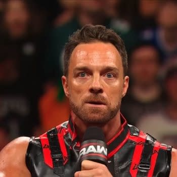 LA Knight stands in the ring on WWE Raw, holding a microphone and looking intensely at the crowd. He wears a black-and-red outfit against a blurred arena audience.