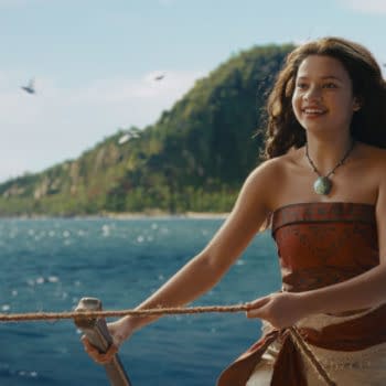 Catherine Laga'aia as Moana smiles while steering a boat across the ocean in Disney's live-action Moana, with tropical islands in the background.