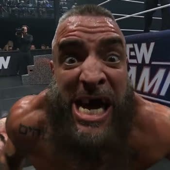 Mark Briscoe yells intensely into the camera at ringside during AEW Dynamite, with a fallen opponent behind him. The AEW Summer Blockbuster backdrop is visible in the background.