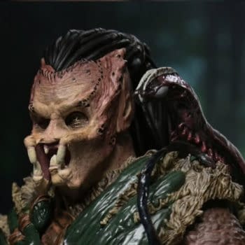 NECA Predator: Badlands Ultimate Dek (Bone Bison Armor) figure shown in a close-up, with the armored Predator character wearing a bone-like face mask and green textured armor. The dark background gives the collectible a dramatic display look.
