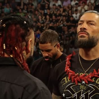 Roman Reigns stands face to face with Jacob Fatu in the WWE Raw ring, both wearing black shirts and intense expressions. The crowd watches behind them as the confrontation unfolds.