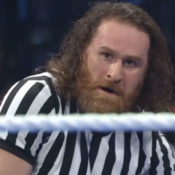 Sami Zayn, wearing a referee shirt, looks intensely toward the action inside the wrestling ring during a WWE title match. The blurred ring rope crosses the foreground.