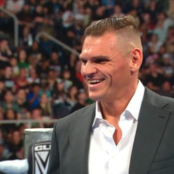 Gunther smiles in a suit inside the WWE ring during SmackDown, appearing amused as the crowd looks on.