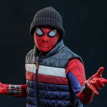 Hot Toys Deluxe Spider-Man 1/6th scale figure wearing a knit beanie and puffer vest, posed against a dark background. The masked Spider-Man holds both hands out in a dynamic pose.