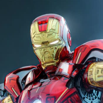 Hot Toys Iron Man Mark VII figure in a red-and-gold Exo-Chrome finish, posed with one arm extended. The glowing eyes and metallic detailing stand out against a dark background.