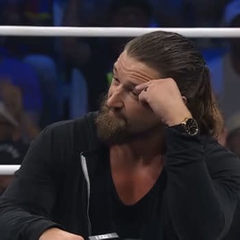 Jay White sits in the AEW ring with his hand to his temple, wearing a black jacket and watch, as the crowd looks on. The Upper Deck logo appears in the corner.