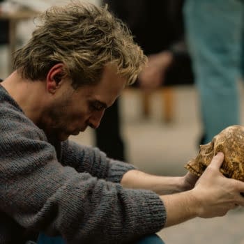 Andrew Scott, in character from Elsinore, bows his head while holding a weathered human skull in both hands.