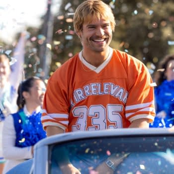 David Corenswet smiles in an orange Irrelevant No. 335 jersey as confetti falls around him at a celebratory parade.