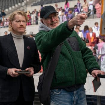 Jesse Plemons stands beside director Francis Lawrence on the set of The Hunger Games: Sunrise on the Reaping, with Lawrence pointing toward a camera in a stadium filled with extras.