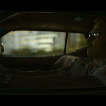 Brad Pitt as Cliff Booth drives at night in a dimly lit car, smoking a cigarette.