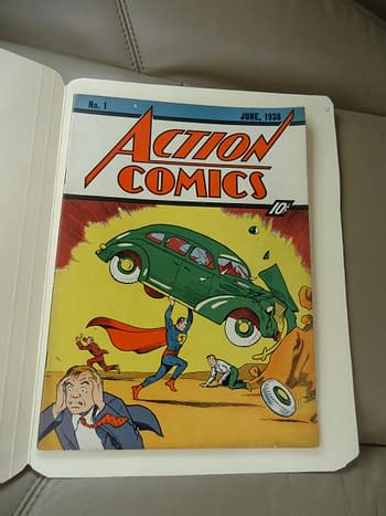Action Comics #1 (DC Comics, 1938). A colorful comic book cover featuring Superman lifting a green car while others react in surprise. The title 'Action Comics' is prominently displayed at the top, with a publication date of June 1938.