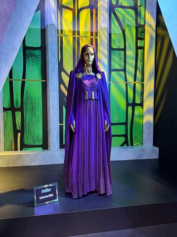 A Latverian Witch costume display at SDCC, featuring a purple hooded robe and metallic mask on a stage-like set.